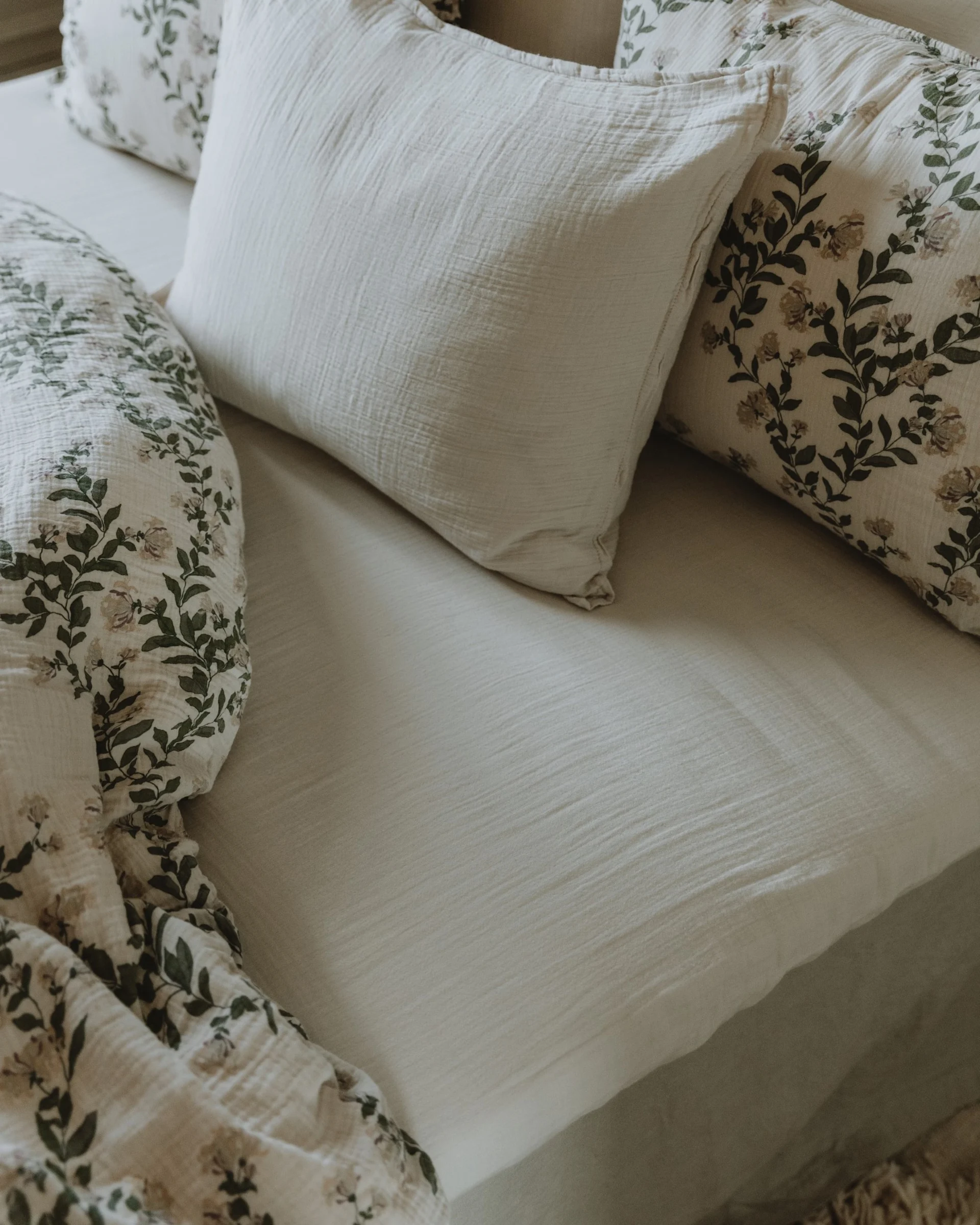 浅米色床,配有柔软有质感的纯色床单和带有绿叶花卉图案的枕头.